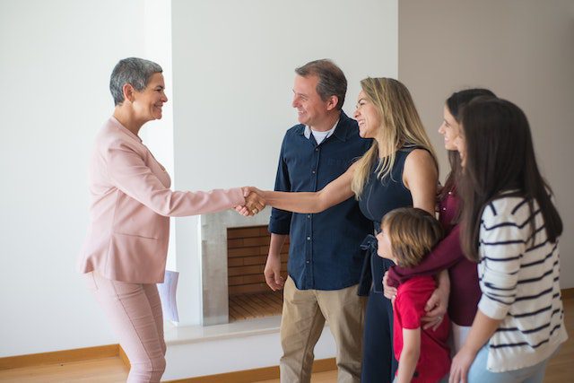 a-person-in-a-pink-suit-shakes-hands-with-a-happy-family-of-four-inside-a-bright-empty-home