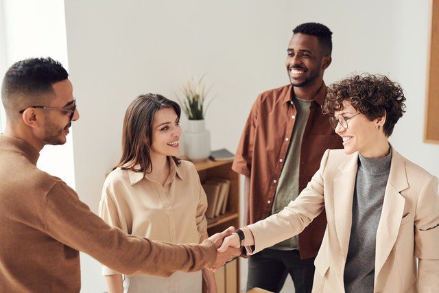 four-people-in-a-bright-office-setting-smiling-and-talking-two-of-them-are-shaking-hands