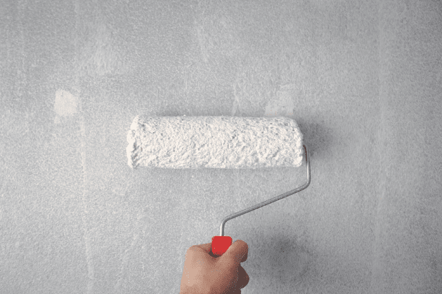 hand-holding-a-paint-roller-applying-white-paint-to-a-wall