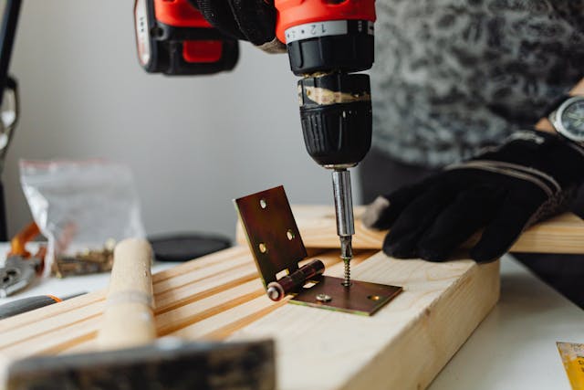 person-using-power-drill-to-attach-hinge-to-wood