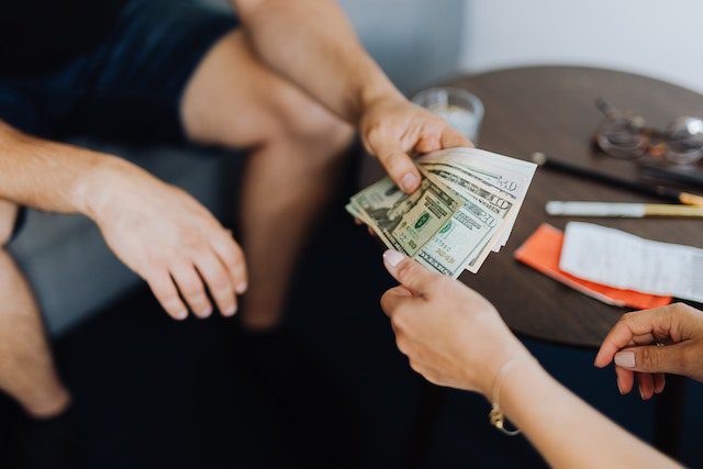 two-people-exchanging-cash-while-sitting-near-a-small-table